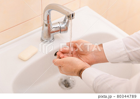 hand washing with soap or gel under running water in the washbasin, cleanliness and hygiene, men's hands dressed in a white shirt hand washing with soap or gel under running water in the washbasin, cleanliness and hygiene, men's hands dressed in a white shirt 80344789