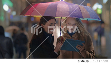 Female friends using touch pad on rainy evening in city Female friends using touch pad on rainy evening in city 80348286