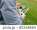 Man remotely operating flying quadcopter drone using smartphone screen. Close up of hands of drone pilot. 80348684