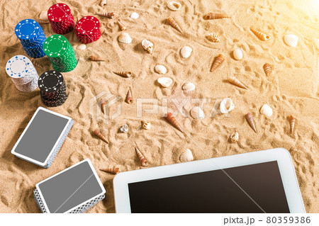 Gambling on vacation concept - white sand with seashells , colored poker chips and cards. Top view Gambling on vacation concept - white sand with seashells , colored poker chips and cards. Top view 80359386