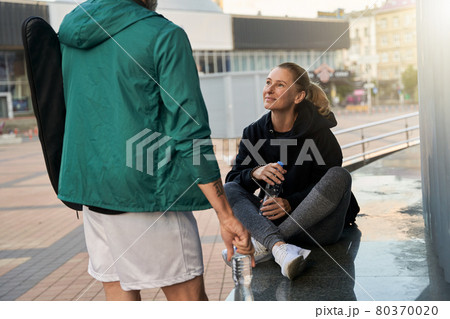 Sportive mature woman woman in sportswear talking with her partner outdoors while waiting together for workout 80370020