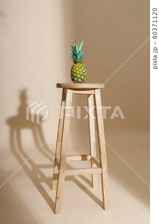 Studio shot of fresh and sweet whole pineapple fruit with leaf on chair isolated over beige background Studio shot of fresh and sweet whole pineapple fruit with leaf on chair isolated over beige background 80371120