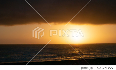 Moody sunrise shot with calm ocean, sun and thick cloud layer in upper third, shot in Kaikoura, New Zealand 80374355