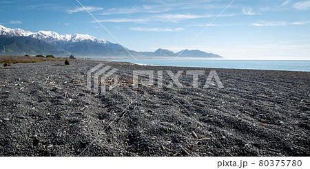 Remote beach with black gravel, azure waters, blue skies and mountains in backdrop. Shot at Kaikoura peninsula, New Zealand 80375780