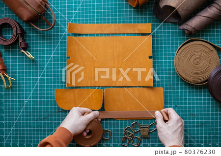 Process cutting scheme of bag with equipment and materials. Male tanner working at leather workshop Process cutting scheme of bag with equipment and materials. Male tanner working at leather workshop 80376230