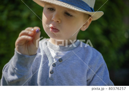 Little boy in stylish straw hat picks honeysuckle berry Little boy in stylish straw hat picks honeysuckle berry 80376257
