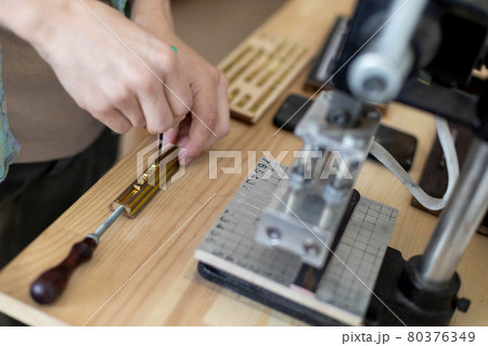Closeup craftsman hands typing text for branding leather with personal stamp. Creating craft label 80376349