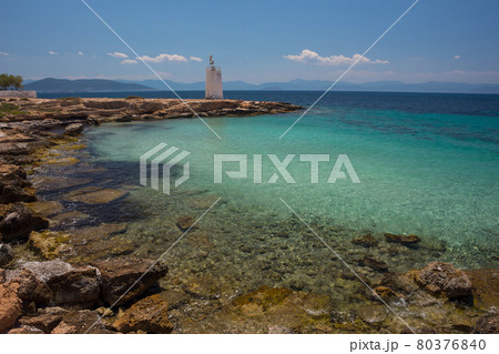 The wild coast of Aegina island with clear and blue waters of Mediterranean sea and the old small lighthouse in the background, in Saronic gulf, Greece. 80376840