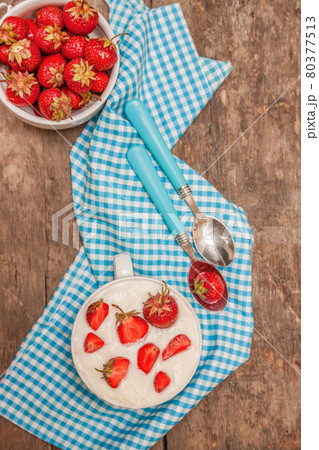 In a cup of yogurt and fresh strawberries, on a blue spoon towel In a cup of yogurt and fresh strawberries, on a blue spoon towel 80377513