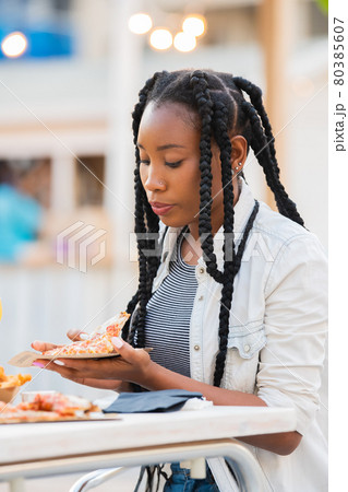 Afro american woman picking up a pizza slice at an outdoors terrace 80385607