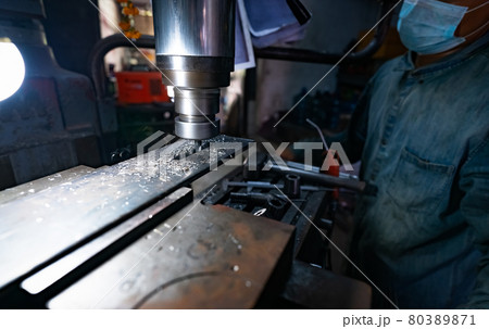 A man wear surgical mask working with milling machine. Tool for cut metal workpiece. Vertical milling machine with cemented carbide milling cutter. Steel manufacturing industry. Milling process. A man wear surgical mask working with milling machine. Tool for cut metal workpiece. Vertical milling machine with cemented carbide milling cutter. Steel manufacturing industry. Milling process. 80389871