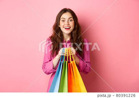 Young beautiful lady going on shopping, holding bags and smiling excited, buying with discounts, standing against pink background Young beautiful lady going on shopping, holding bags and smiling excited, buying with discounts, standing against pink background 80391226
