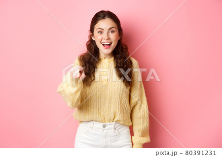 Young brunette woman laughing, smiling amazed and pointing at camera, choosing you, standing against pink background Young brunette woman laughing, smiling amazed and pointing at camera, choosing you, standing against pink background 80391231