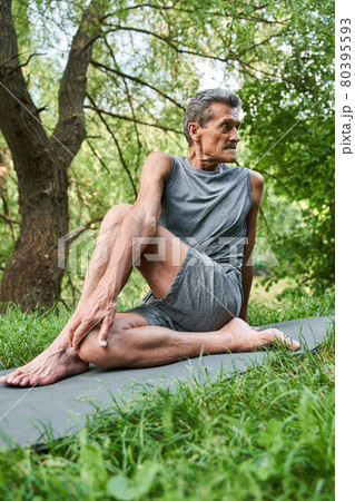 Man stretching his legs while sitting at the mat and doing workout at the nature Man stretching his legs while sitting at the mat and doing workout at the nature 80395593