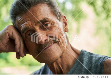 Man looking at the camera with pleasure smile while leaning at the trunk of the tree 80395613
