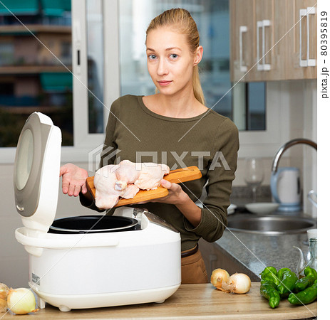 Smiling woman cooking with electric multicooker at home kitchen 80395819
