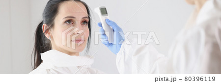 For doctor in protective suit, body temperature is measured with thermometer after work shift 80396119