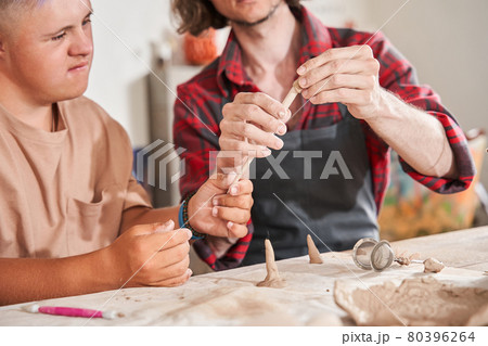 Man with special needs working with clay in ceramic studio under supervision of craftsman Man with special needs working with clay in ceramic studio under supervision of craftsman 80396264
