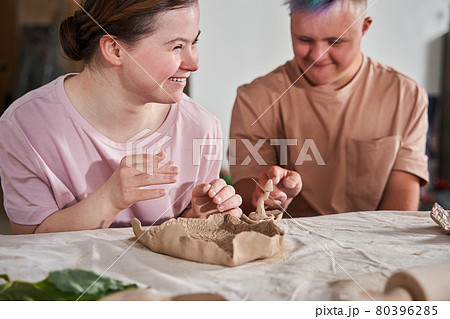 Girl with down syndrome laughing out loud and looking away while making plates from clay Girl with down syndrome laughing out loud and looking away while making plates from clay 80396285