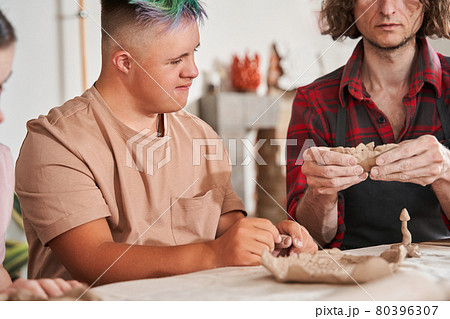 Sculptor preparing shape of the future plate and showing it to his students with special needs 80396307