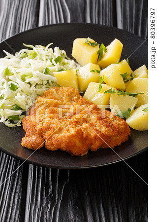 Kotlet Schabowy Polish Breaded Pork Chop with boiled potatoes and cabbage salad close-up in a plate. Vertical 80396797