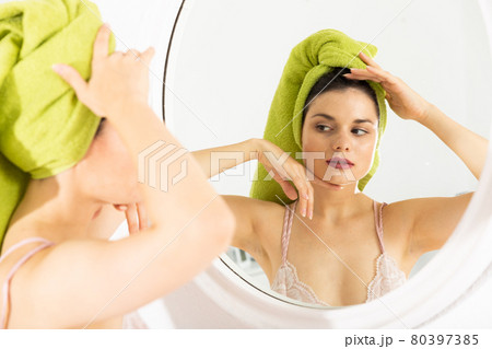 Young female touching face, using mirror in bedroom Young female touching face, using mirror in bedroom 80397385
