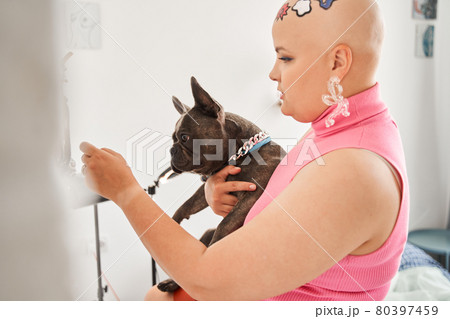 Woman wearing jewelry holding at hands her french bulldog while looking at the mirror 80397459