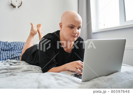 Woman laying at her stomach at the bed and looking at the digital screen of her laptop Woman laying at her stomach at the bed and looking at the digital screen of her laptop 80397648