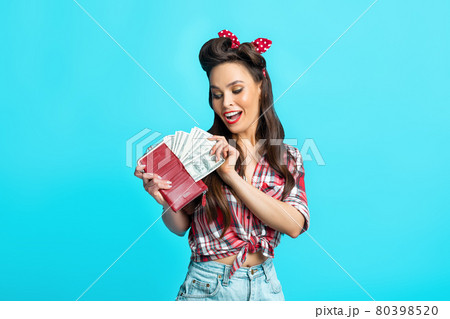 Joyful pinup lady in retro wear taking money from full wallet on blue studio background. Wealth, income, big win Joyful pinup lady in retro wear taking money from full wallet on blue studio background. Wealth, income, big win 80398520