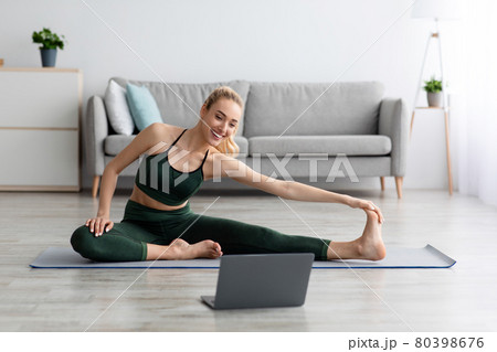 Young blonde sports woman in sportswear doing workout on floor at home and watching fitness videos in laptop 80398676