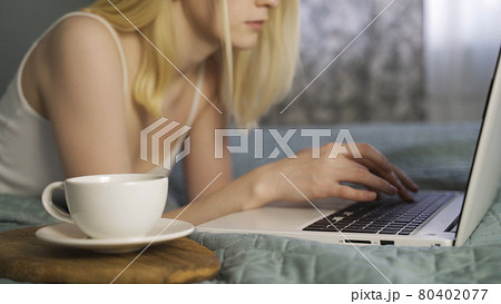 Young woman lying on bed using notebook computer and typing. 80402077