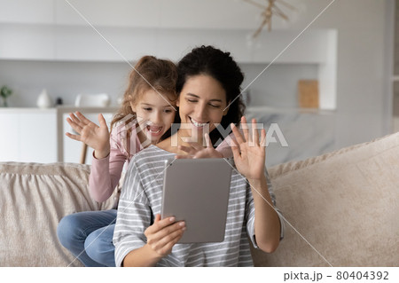 Smiling Latino mom and daughter talk on video call on pad Smiling Latino mom and daughter talk on video call on pad 80404392