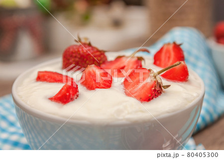 In a cup of yogurt and fresh strawberries, on a blue spoon towel, scattered strawberries, on a wooden background. Close-up, top view.Concept healthy and healthy breakfast 80405300