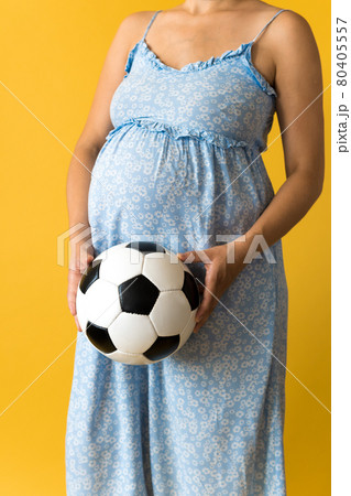 Motherhood, femininity, football, sport, dairy, hot summer. croped unrecognizable pregnant young pretty woman in floral blue dress holds soccer white and black ball rubs tummy on yellow background Motherhood, femininity, football, sport, dairy, hot summer. croped unrecognizable pregnant young pretty woman in floral blue dress holds soccer white and black ball rubs tummy on yellow background 80405557