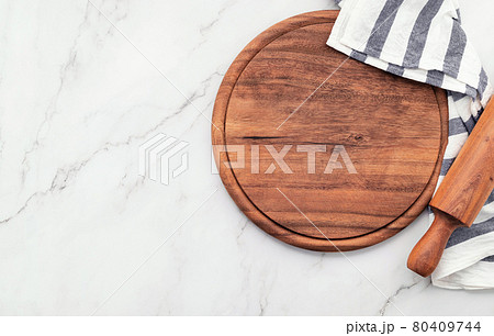 Empty wooden pizza platter with napkin and rolling pin set up on marble stone kitchen table. Pizza board and tablecloth on white marble background. 80409744