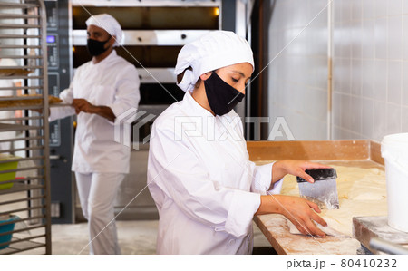 Bakery worker cuts raw dough with knife 80410232