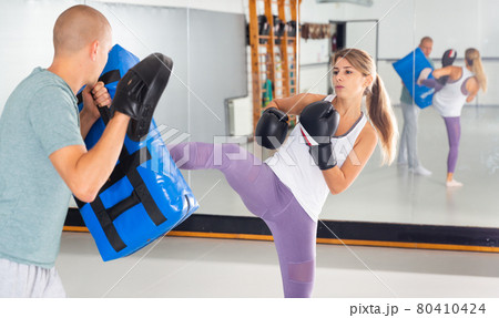 Determined woman kicking boxing shield during self-defense course Determined woman kicking boxing shield during self-defense course 80410424