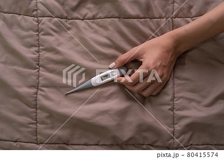 Hands hold a medical thermometer isolated on bed in bedroom at home. Fever or Diagnosis self check up. Medical and healthcare equipment. Coronavirus covid-19 outbreak. 80415574