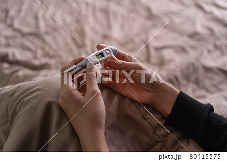 Hands hold a medical thermometer isolated on bed in bedroom at home. Fever or Diagnosis self check up. Medical and healthcare equipment. Coronavirus covid-19 outbreak. 80415575