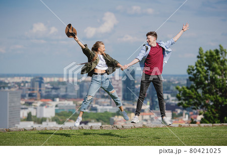 Cheerful young couple travelers in city on holiday, jumping. Cityscape in the background. 80421025