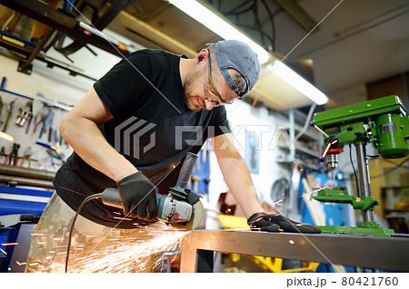 Metalwork craftsman cutting metal with grinder tools. Worker man in protection gloves and glasses working in the workshop. Small local business. Metalwork craftsman cutting metal with grinder tools. Worker man in protection gloves and glasses working in the workshop. Small local business. 80421760
