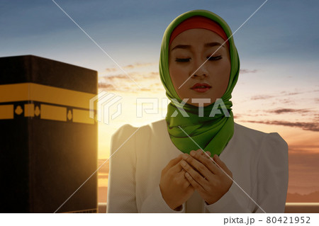 Asian Muslim woman in a veil standing and praying with Kaaba view Asian Muslim woman in a veil standing and praying with Kaaba view 80421952