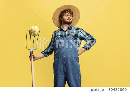 Portrait of young man, farmer with garden equipment isolated over yellow studio background. Concept of professional occupation, work. Portrait of young man, farmer with garden equipment isolated over yellow studio background. Concept of professional occupation, work. 80422060