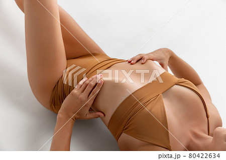 Cropped slim fitness female body in mustard swimsuit llying on floor over white studio background. Cropped slim fitness female body in mustard swimsuit llying on floor over white studio background. 80422634