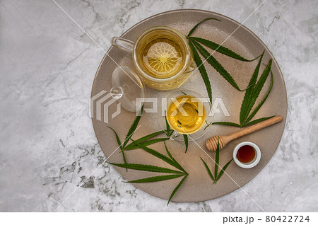 Refreshing and enjoy with A cup of Cannabis herbal tea and Stem with green marijuana leaves with honey on marble table. Refreshing and enjoy with A cup of Cannabis herbal tea and Stem with green marijuana leaves with honey on marble table. 80422724