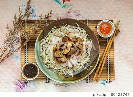 Braised pork, tofu, crisp squid in sweet soy sauce served on Chinese steamed rice noodles and bean sprout in ceramic plate. 80422747