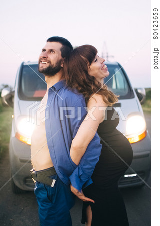 A married couple who are expecting a baby are photographed at sunset in a flower field. A pregnant woman and her loving man. The father kisses the belly in which his child is. Last terms of pregnancy 80423659