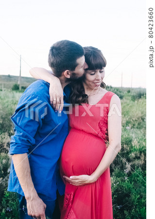 A married couple who are expecting a baby are photographed at sunset in a flower field. A pregnant woman and her loving man. The father kisses the belly in which his child is. Last terms of pregnancy 80423660