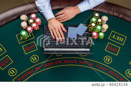 Closeup of poker player with playing cards, laptop and chips Closeup of poker player with playing cards, laptop and chips 80428116