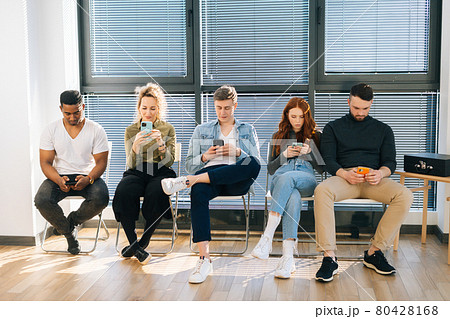 Front view of group five young diverse ethnicity candidates using mobile phones while waiting job interview in modern office lobby. Front view of group five young diverse ethnicity candidates using mobile phones while waiting job interview in modern office lobby. 80428168